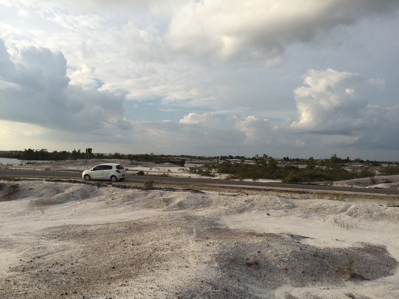 A consequence of the gold rush at Kereng Pangi is barren lands devoid of vegetation. (Semiarto A Purwanto) A car zooms by on a road in a barren landscape.